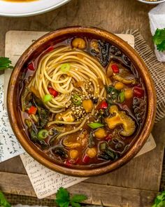 a bowl filled with noodles and vegetables on top of a wooden table next to some napkins