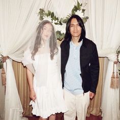 a man and woman standing next to each other in front of white drapes with flowers on them