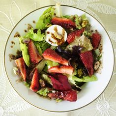 a salad with strawberries, lettuce and eggs in it on a white plate