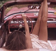 a woman laying in the drivers seat of a car with her feet up on the steering wheel