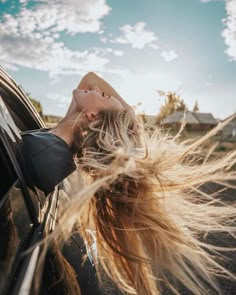 a woman with long hair sticking her head out the window of a car on a sunny day