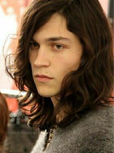 a young man with long hair is looking at the camera while standing in front of other people