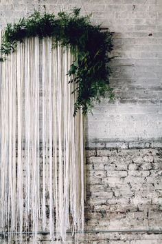 a wall hanging with plants on it in front of a brick wall that is covered in white string