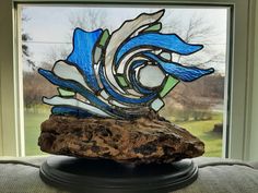 a piece of stained glass sitting on top of a wooden block in front of a window