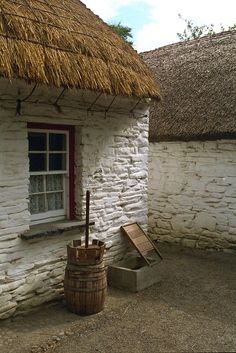 an old thatched roof house with a wooden barrel next to it and a window