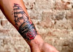 a person's arm with a ship tattoo on it and a rose in the middle