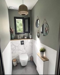 a white toilet sitting next to a window in a bathroom under a light fixture with three mirrors on the wall