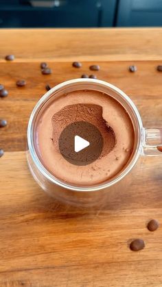 a person is holding a cup of hot chocolate in front of coffee beans on a wooden table