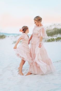 mother and daughter in pink dresses walking on the beach at sunset with sand dunes behind them