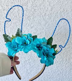 a hand holding a headband with blue flowers on it and two green leaves in the middle