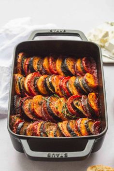 a pan filled with grilled vegetables on top of a white table next to bread