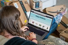 a woman is sitting on the couch with her laptop in front of cardboard boxes that are stacked up behind her