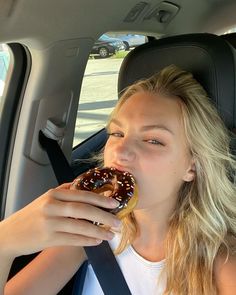 a woman sitting in the back seat of a car eating a donut