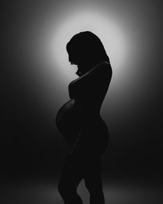 a pregnant woman is silhouetted against a dark background