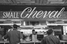 black and white photograph of people in front of small cheesy restaurant with large sign