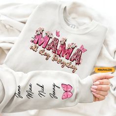 a person holding a white shirt with pink butterflies on it and the words mama is always in cursive writing