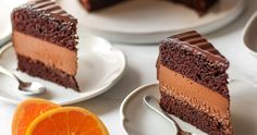 three slices of chocolate cake on white plates with oranges and spoons next to them