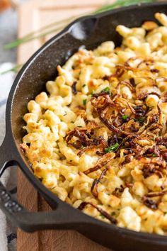 a skillet filled with macaroni and cheese on top of a wooden cutting board