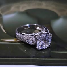 an engagement ring with two diamonds on it sitting on top of a green box in front of a glass display case