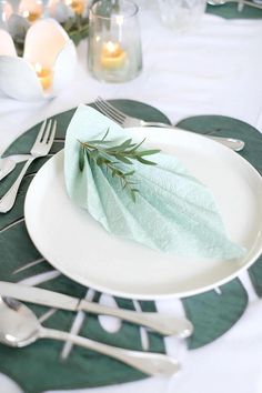 a white plate topped with a leaf on top of a green table cloth next to silverware