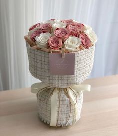 a bouquet of pink and white roses in a basket on a table with a tag