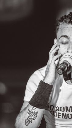 a man with tattoos on his arm holding a microphone up to his face and covering his mouth