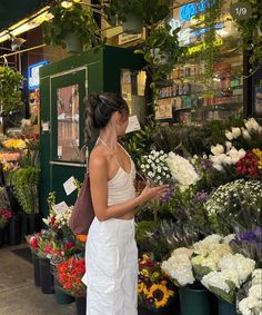 a woman in white dress looking at flowers