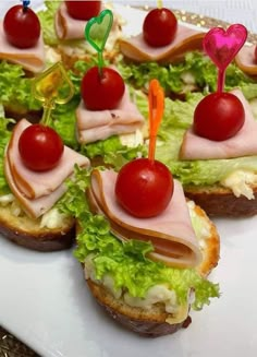 small sandwiches with meat, cheese and cherry tomatoes on them sitting on a white plate