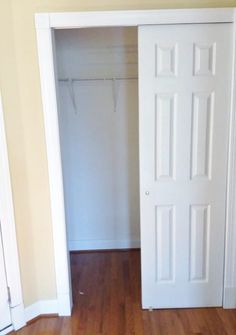 an empty room with white doors and hard wood flooring on one side, another door is open to reveal the closet