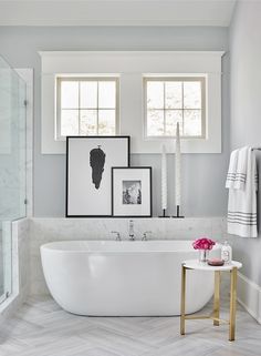 a white bath tub sitting in a bathroom next to two pictures hanging on the wall