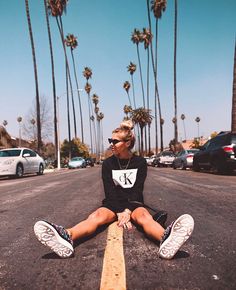 a woman sitting on the side of a road with palm trees in front of her