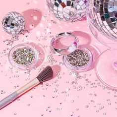 various glitters and makeup brushes on a pink surface with disco balls in the background