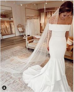 a woman in a white wedding dress is looking down at her veil as she walks through the store