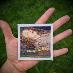 a hand holding up a small cross stitch picture