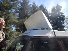 an older man standing next to a parked car with the hood up on it's roof