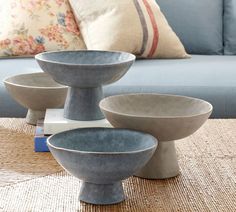 three gray bowls sitting on top of a table next to a blue couch and pillows