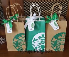 three starbucks bags sitting on top of a wooden table next to a christmas tree with green bows