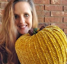 a woman holding a large knitted pumpkin in front of her face and smiling at the camera