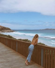 a woman standing on a wooden deck next to the ocean looking out at the water