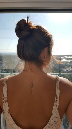 a woman with a flower tattoo on her back standing in front of a window looking out at the city