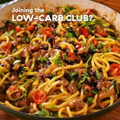 a skillet filled with pasta and vegetables on top of a wooden table