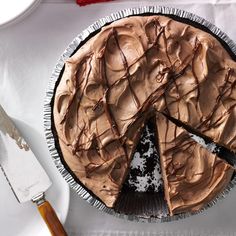 a chocolate pie with one slice missing from it on a plate next to a knife