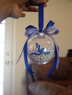 a hand holding a glass ornament with a blue ribbon