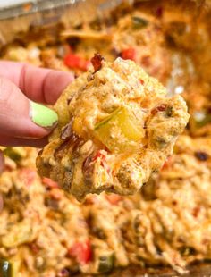 a hand holding up a cracker over a casserole dish filled with meat and vegetables