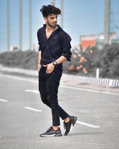 a young man is walking down the street in black pants and a blue shirt with his hair pulled back