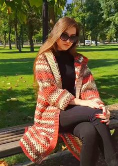 a woman sitting on top of a wooden bench wearing sunglasses and a crocheted jacket