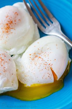 two fried eggs on a blue plate with mustard and seasoning next to a fork