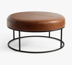 a brown leather ottoman sitting on top of a black metal frame table with a round base