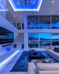 a living room with white couches and blue lighting on the ceiling is lit up by recessed lights