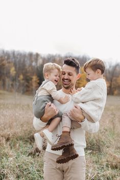 a man holding two boys in his arms while standing in a field with tall grass